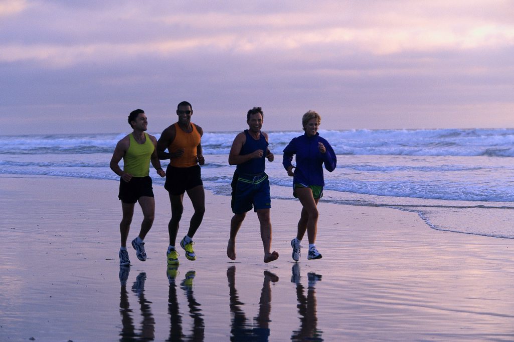 exercize beach sand ocean Four runners jog along a beach at sunset, reflecting on the wet sand.