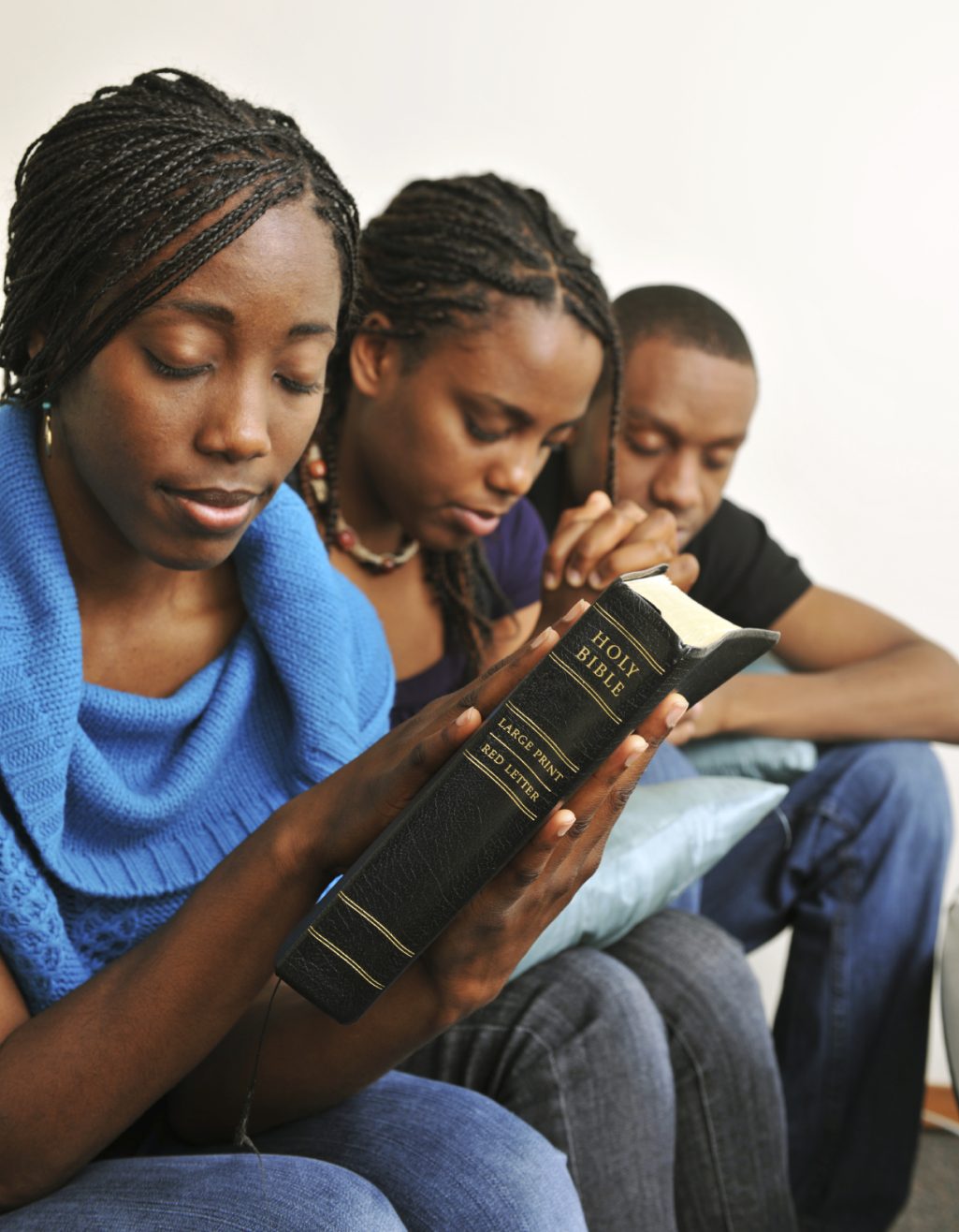 Family Prayer & Bible Study Togetherness Three people engaged in reading a book, focused and thoughtful.